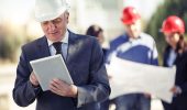 Man in a suit and hard hat smiles at an ipad.