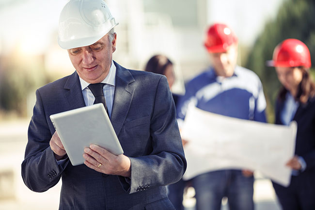 Man in a suit and hard hat smiles at an ipad.