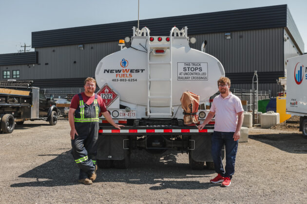 Two young men stand in front of a truck.